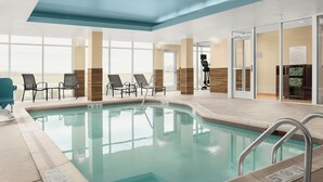 Ein Hallenbad mit klarem Wasser, umgeben von Liegestühlen und einem Umkleideraum.