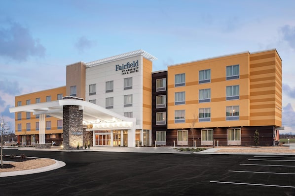 A Fairfield Inn & Suites hotel with a modern design, featuring a central entrance with a covered walkway, multiple floors, and a parking lot in front.