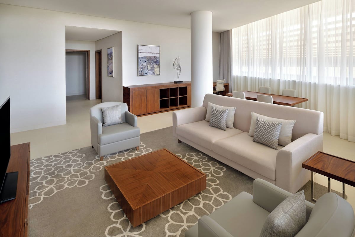 A modern living room with a sofa, armchairs, a coffee table, and a dining area with a table and chairs.