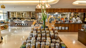A buffet area with a variety of food items in glass jars, a central floral arrangement, and a kitchen area in the background. - Marriott Riyadh Diplomatic Quarter (Riyadh)