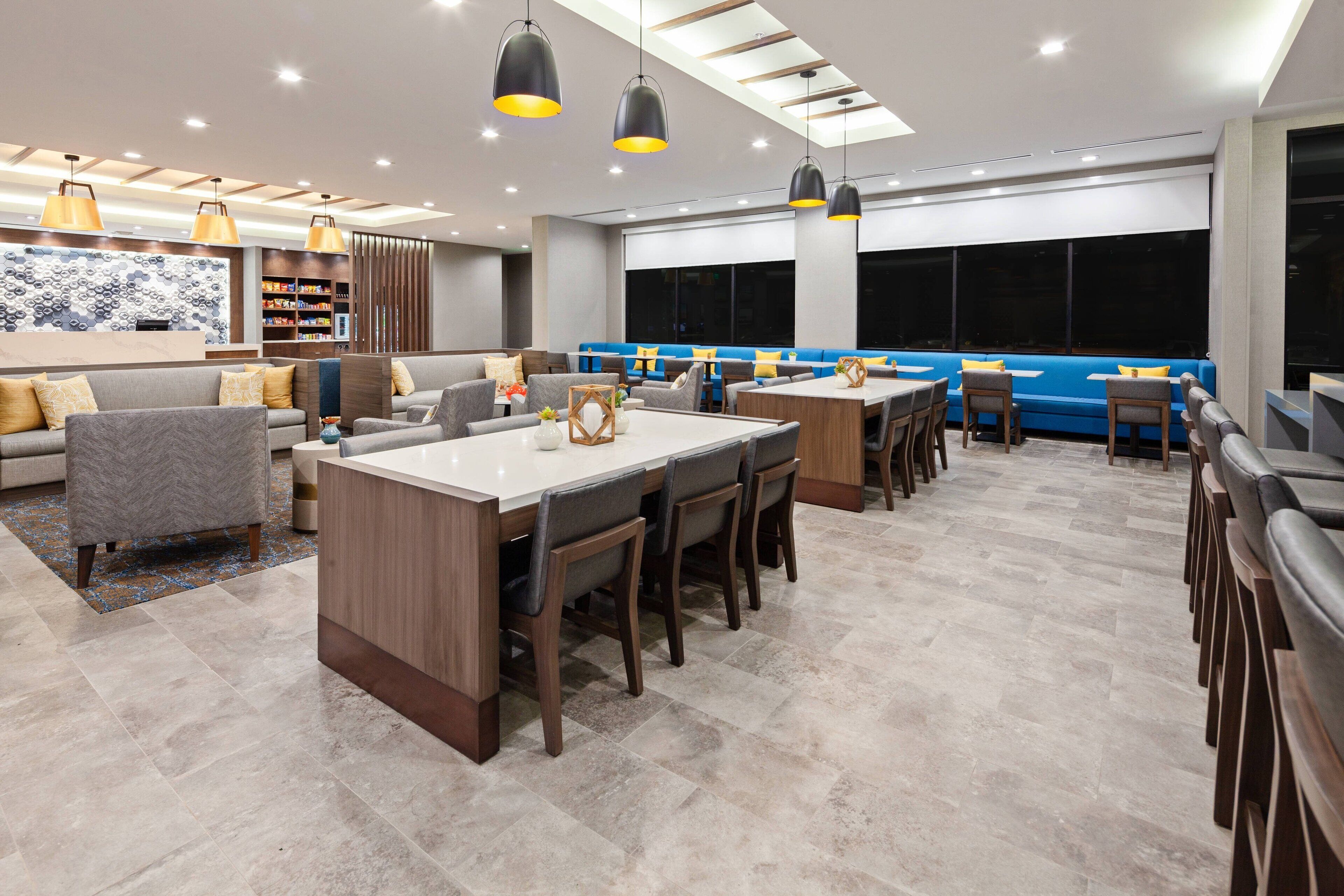 Un moderno vestíbulo de hotel con una zona de estar central, un bar y un comedor.