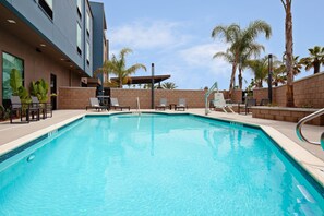 A swimming pool with lounge chairs and a covered area, surrounded by palm trees and a modern building. - SpringHill Suites by Marriott Escondido Downtown (Escondido)