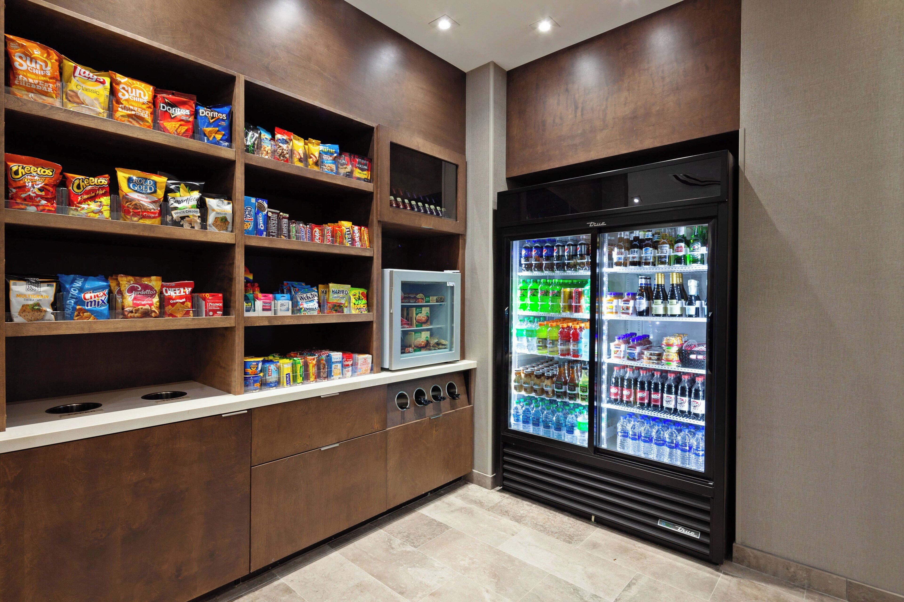 Espaço com lanches e bebidas, incluindo prateleiras de petiscos e um refrigerador de bebidas.