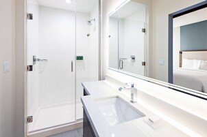 Un baño moderno con ducha envuelta en vidrio, un espejo grande y un lavabo blanco.