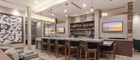 A modern bar area with a long counter, multiple bar stools, and a television mounted on the wall.