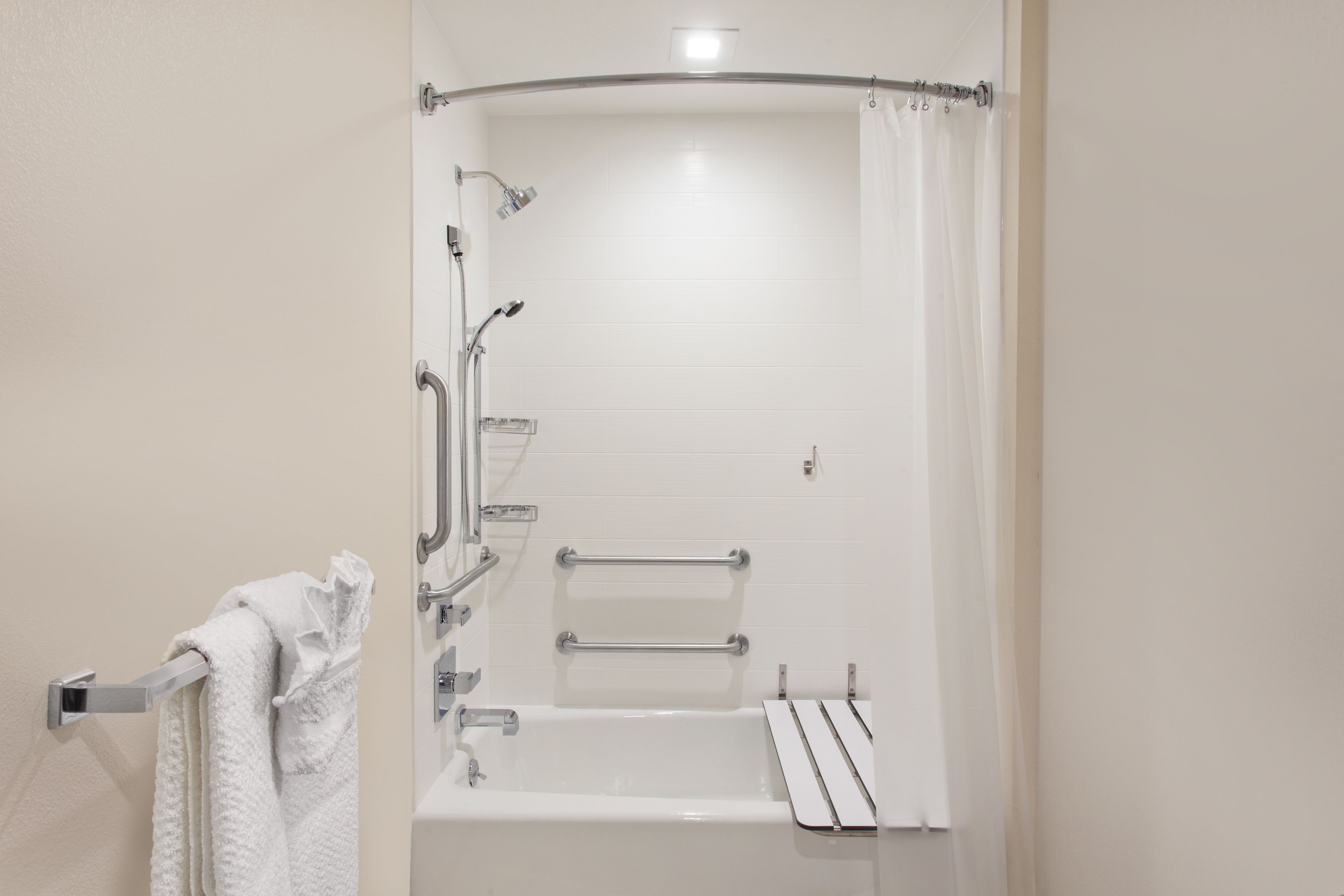 Un baño moderno con cabina de ducha, barras de apoyo y un perchero.