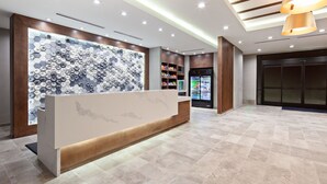 Un espace d’accueil au design moderne, comprenant un comptoir de réception, un mur orné d’un motif hexagonal et un réfrigérateur rempli de boissons.
