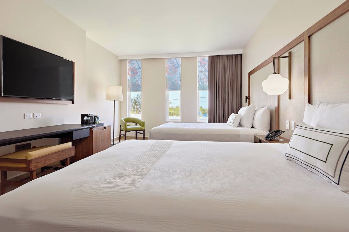 Ein Hotelzimmer mit einem großen Bett, einem Schreibtisch, einem Stuhl, einem Fernseher und einem Fenster mit Vorhängen.