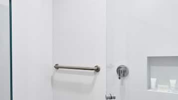 Une douche moderne dotée d’une porte en verre, d’une barre d’appui et d’une étagère pour les articles de toilette.