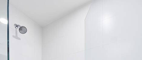 A modern shower with a glass door, a handrail, and a shelf with toiletries.