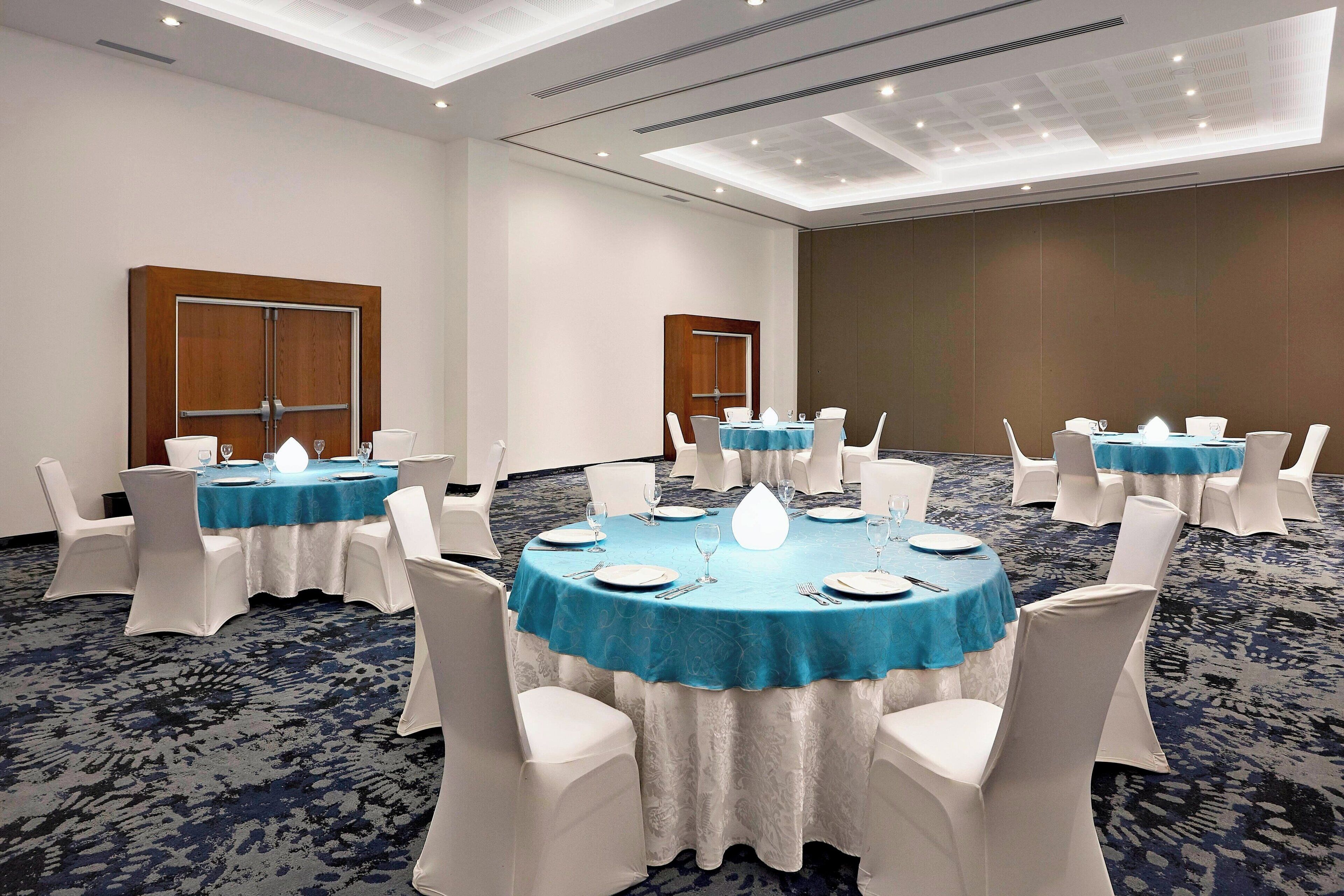 A conference room with round tables, white chairs, and blue tablecloths.