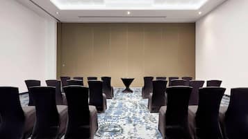 A conference room with rows of chairs, a patterned carpet, and a ceiling with recessed lighting.
