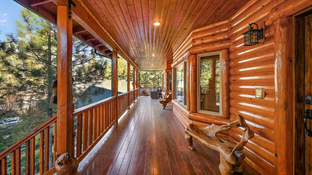 A wooden cabin with a covered porch, large windows, and a view of the surrounding forest.
