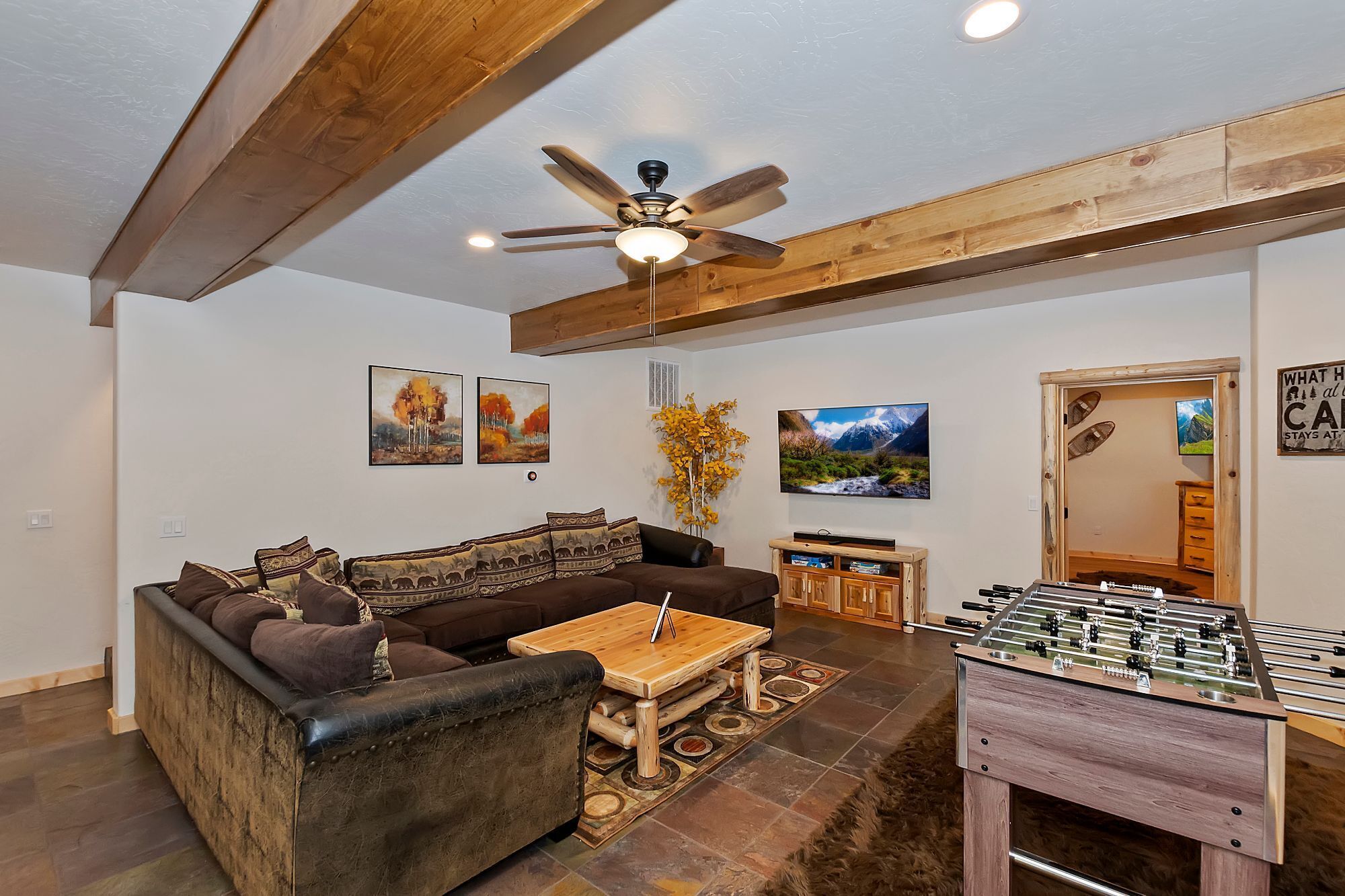 A cozy living room with a sofa, a coffee table, a foosball table, and a ceiling fan.