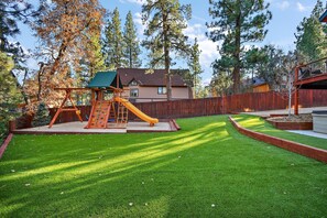 A backyard with a play area, a wooden fence, and a house in the background.