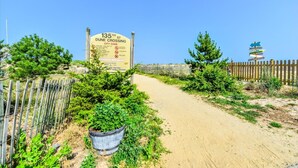 Ein schmutziger Pfad führt zu einem Strandabschnitt, wo ein Schild mit der Aufschrift '135th St. Dune Crossing City Code' und verschiedenen Strandregeln zu sehen ist.