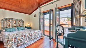 A bedroom with a large bed, a wooden ceiling, a view through a glass door, and a table with chairs. - Música penthouse 360º (Sesimbra)
