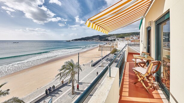 A balcony with a view of the beach, a striped awning, and outdoor furniture. - Música penthouse 360º (Sesimbra)
