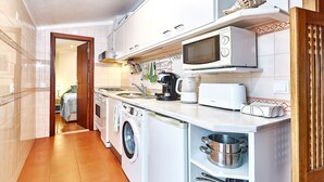 A compact kitchen with a washing machine, microwave, and a coffee maker. - Música penthouse 360º (Sesimbra)