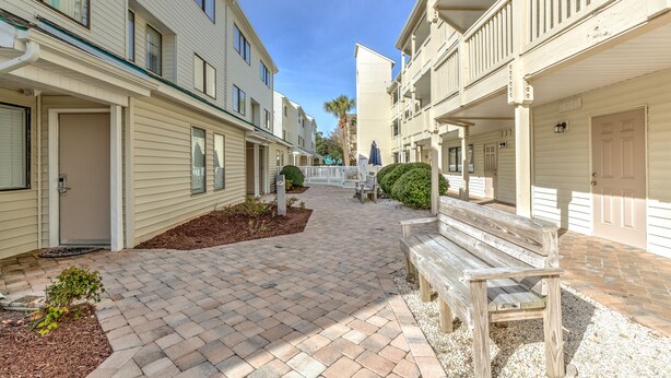 A pathway leading to a row of beachfront condominiums with balconies, a bench, and a small garden area. - Steps to the beach  daily rentals pool washer dryer onsite two balconies full kitchen (Myrtle Beach)