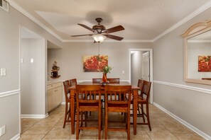 A dining room with a wooden table and chairs, a ceiling fan, and artwork on the walls. - Steps to the beach daily rentals pool washer dryer onsite two balconies full kitchen (Myrtle Beach)