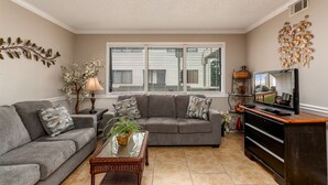 A living room with a grey sofa, a glass coffee table, and a television on a wooden stand. - Steps to the beach  daily rentals pool washer dryer onsite two balconies full kitchen (Myrtle Beach)