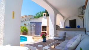 A patio with a pool, outdoor seating, and a view of a building with a tiled wall and a chimney.