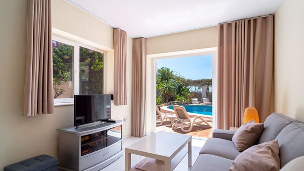 A living room with a TV, a sofa, a coffee table, and a view of an outdoor pool area.