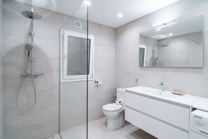 A modern bathroom with a glass-enclosed shower, a toilet, and a white vanity with a mirror.