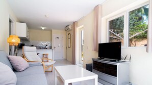 A living room with a sofa, a TV on a stand, a dining table, and a kitchen in the background.