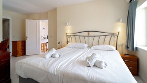 A neatly made bed with towels, a bedside table, a nightstand, a dresser, and an air conditioning unit.