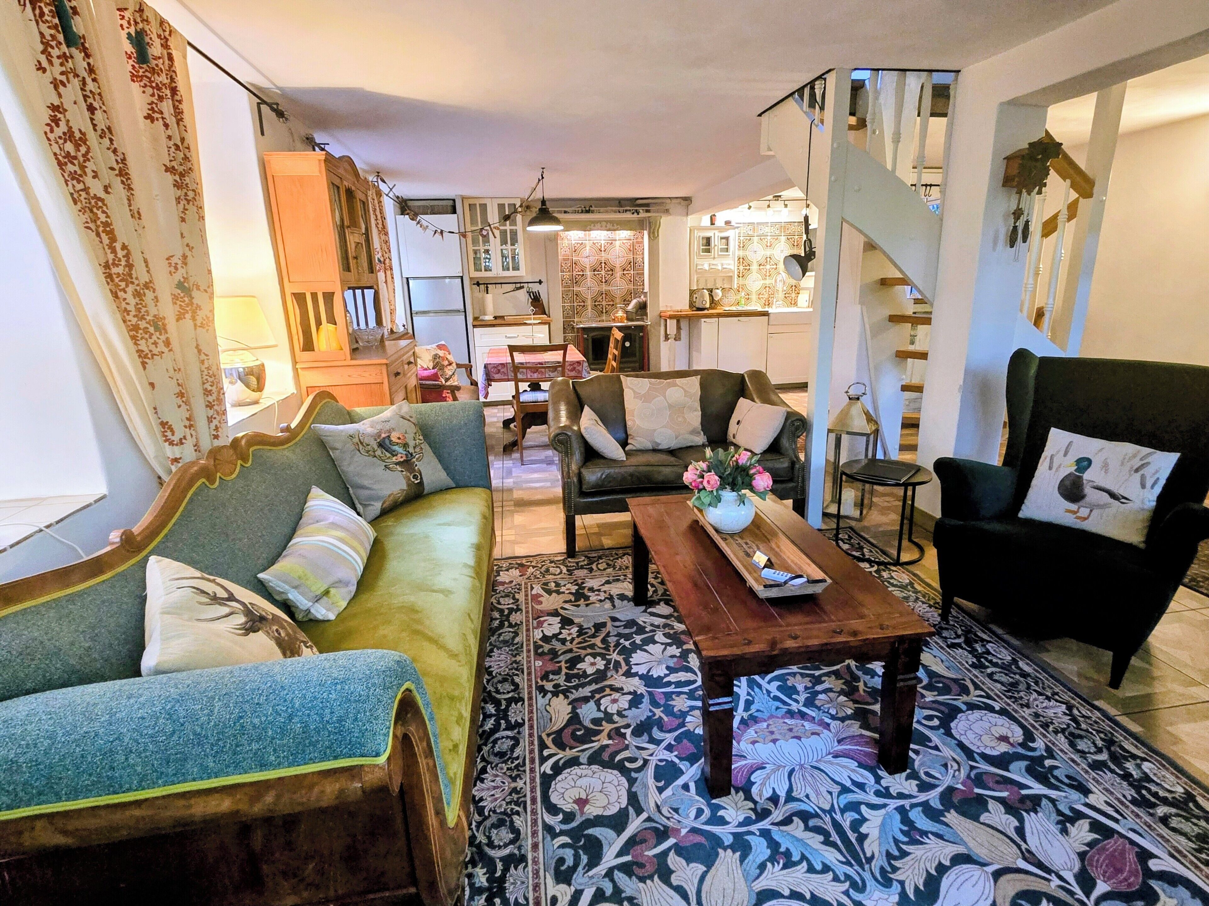 Ein Wohnzimmer mit einer Couch, einem Sessel und einem Couchtisch. Eine Treppe führt zu einer weiteren Ebene.