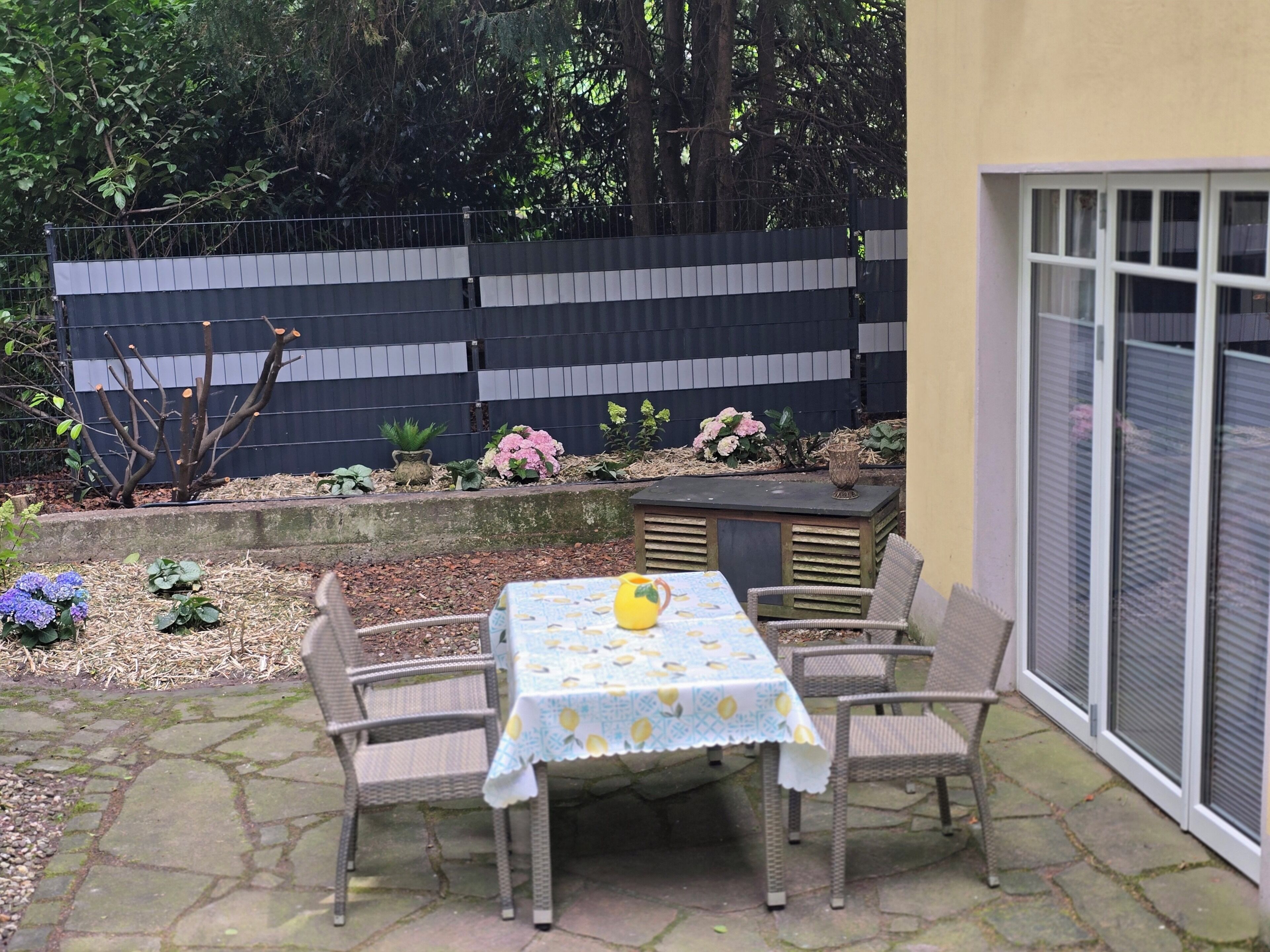 Un patio con mesa y sillas, un pequeño jardín y una cerca.