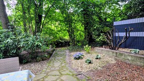 A stone pathway leading through a lush garden with a table and chairs on the left. - HR Cottage am Honigbach in the center of Coesfeld (Coesfeld)