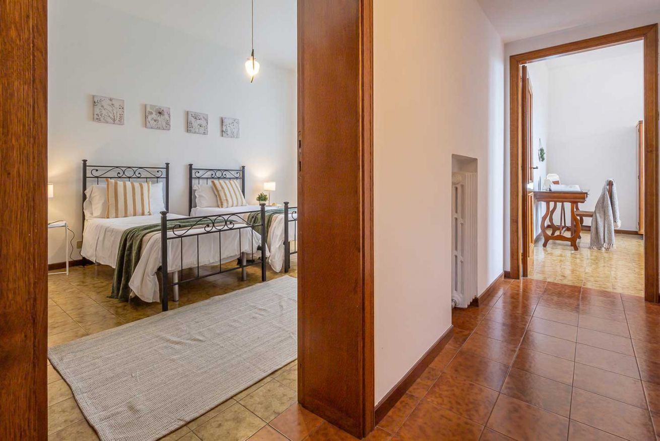 A bedroom with two beds, a wooden door, and a hallway leading to a bathroom.