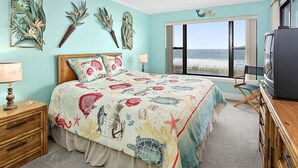 Une chambre à coucher avec un lit, une table de chevet, une commode, un téléviseur et une vue sur la plage.