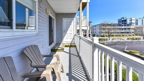 Eine überdachte Veranda mit zwei Adirondack-Stühlen, einer weißen Tür und Blick auf moderne Gebäude im Hintergrund.