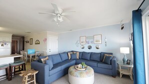 A living room with a blue sectional sofa, a round coffee table, a ceiling fan, and a dining area with a table and chairs. - "Beach Time"  Oceanfront 3 bedroom 3 bath duplex (Holden Beach)