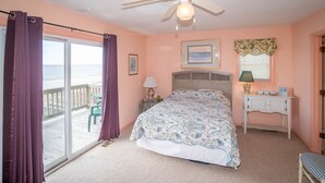 A bedroom with a bed, a nightstand, a desk, a chair, a window with curtains, a ceiling fan, and a view of the outside. - "Beach Time"  Oceanfront 3 bedroom 3 bath duplex (Holden Beach)