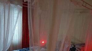Un dormitorio con cama con dosel, mesita de noche y una luz roja al fondo.