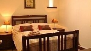 Ein Schlafzimmer mit einem hölzernen Bett, zwei Nachttischlampen, einem gerahmten Bild an der Wand und einem kleinen Tisch neben dem Bett.