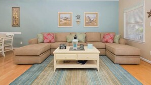 A living room with a sectional sofa, a coffee table, and two wall-mounted picture frames.