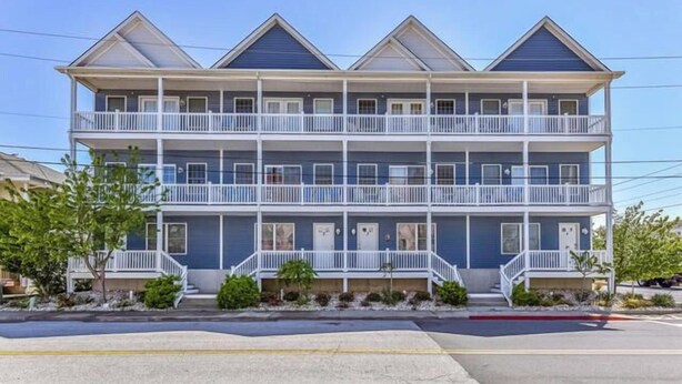 A two-story building with a balcony on each floor, a flat roof, and a clear sky.