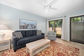 Ein Wohnzimmer mit Sofa, Sessel, Couchtisch und einem Gemälde eines Piers.