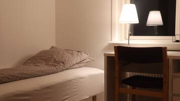 Un letto singolo con coperta a motivi, un comodino con una lampada e una sedia.