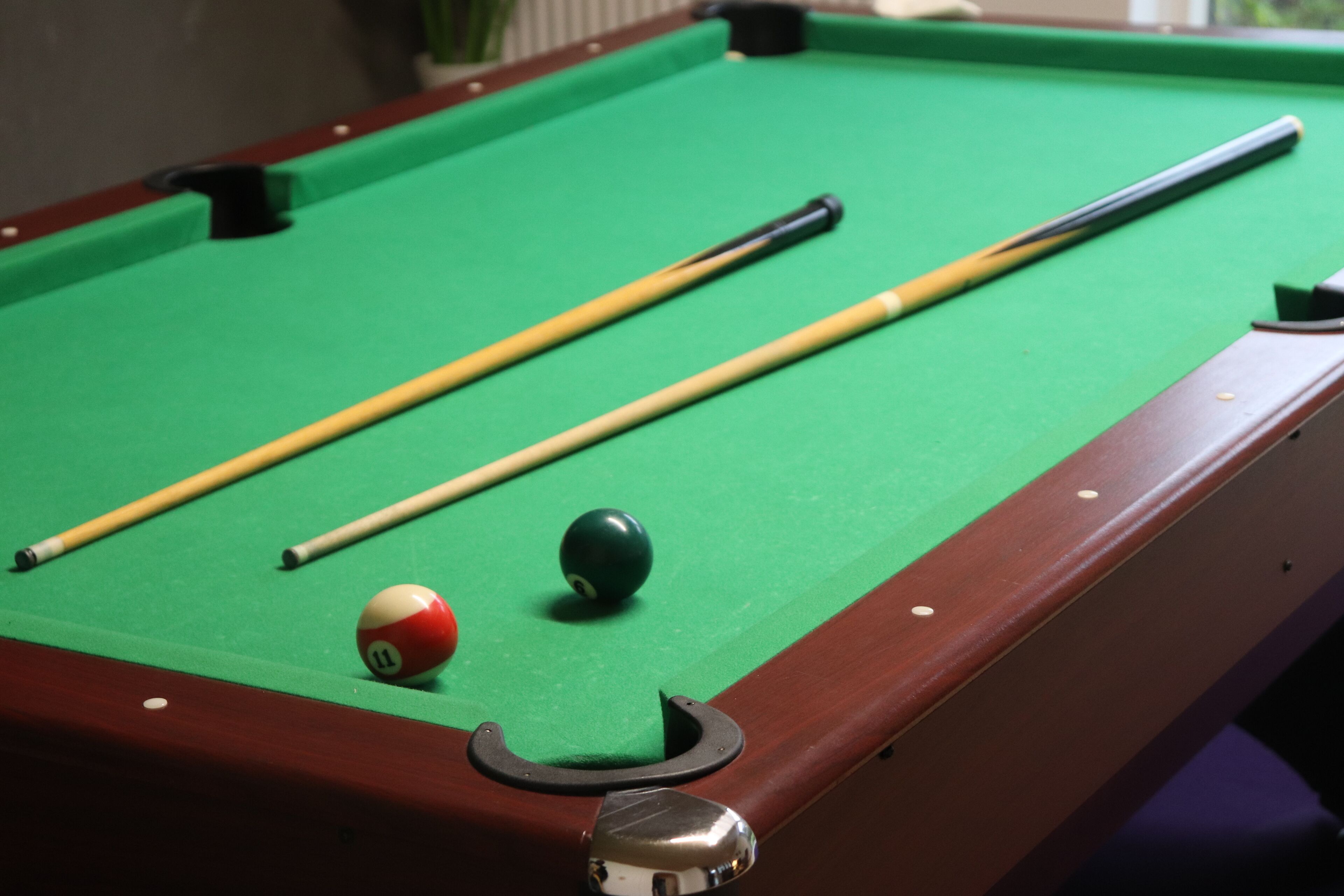 Ein Billardtisch mit grüner Spielbahn, einem Queueschläger, einem Billardball und einem Spielball.