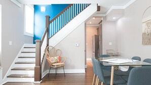 A modern interior with a wooden staircase, a dining area with a glass table, and a kitchen in the background. - Adorable Remodeled Broadripple home walking distance to bars and restaurant.  (Indianapolis)