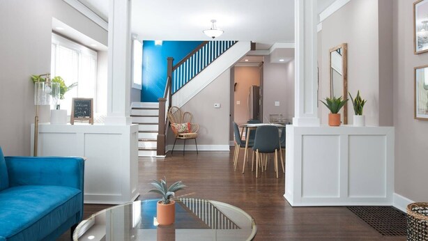 A spacious living room with a blue sofa, a glass coffee table, and a staircase leading to a dining area. - Adorable Remodeled Broadripple home walking distance to bars and restaurant.  (Indianapolis)