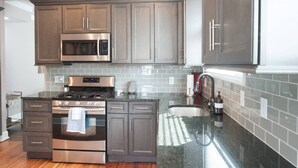 A modern kitchen with stainless steel appliances, grey cabinetry, and a tiled backsplash. - Adorable Remodeled Broadripple home walking distance to bars and restaurant.  (Indianapolis)