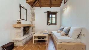 Une pièce chaleureuse avec une cheminée en pierre, un banc en bois, un canapé blanc agrémenté de coussins à motifs et une petite table sur laquelle sont posés un livre et quelques objets décoratifs.